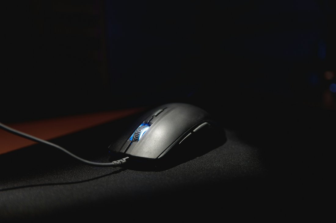 Wired gaming mouse with illuminated scroll wheel on a dark desk surface